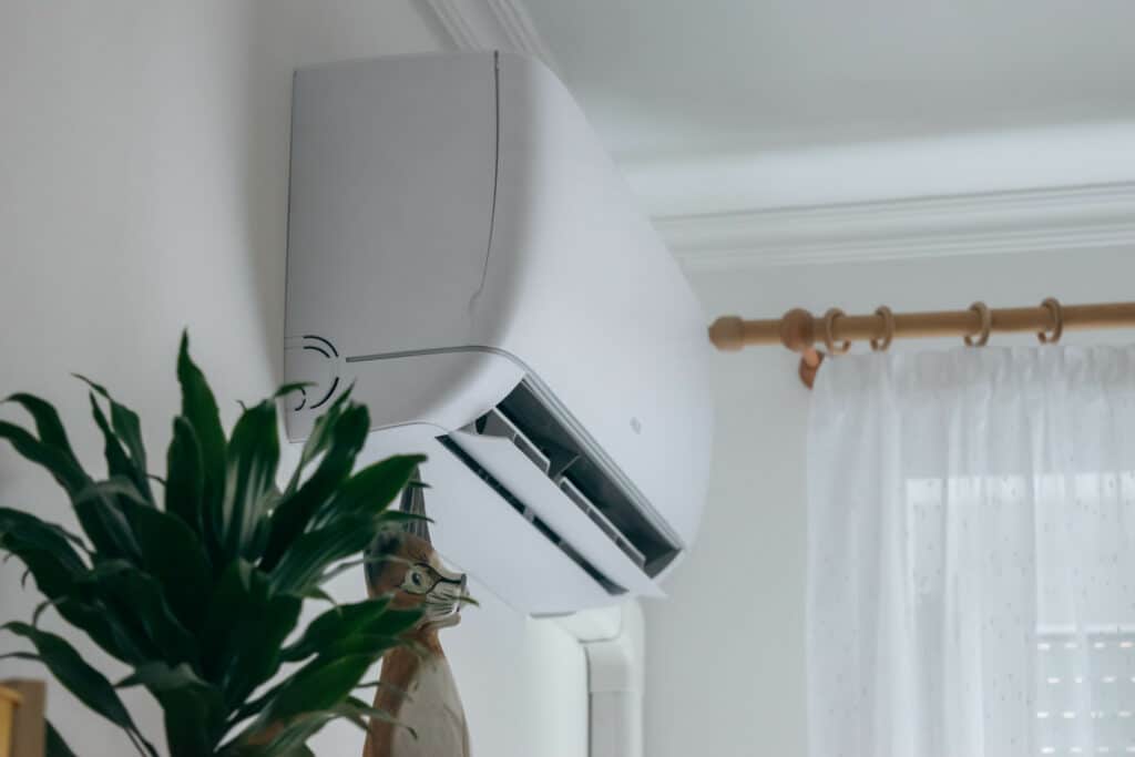 Climatiseur mural blanc intérieur avec plantes et rideaux Climatiseur mural blanc intérieur près d'une plante verte et de rideaux blancs à tringles en bois.